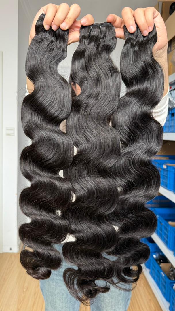 Three long flawless bundles bundles of long, dark brown body wave hair extensions held up by hands in front of a store background.