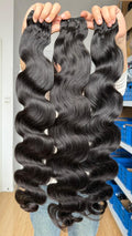 Three long flawless bundles bundles of long, dark brown body wave hair extensions held up by hands in front of a store background.