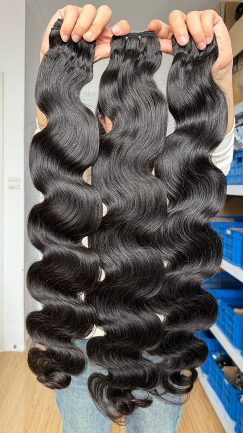 Three long flawless bundles bundles of long, dark brown body wave hair extensions held up by hands in front of a store background.